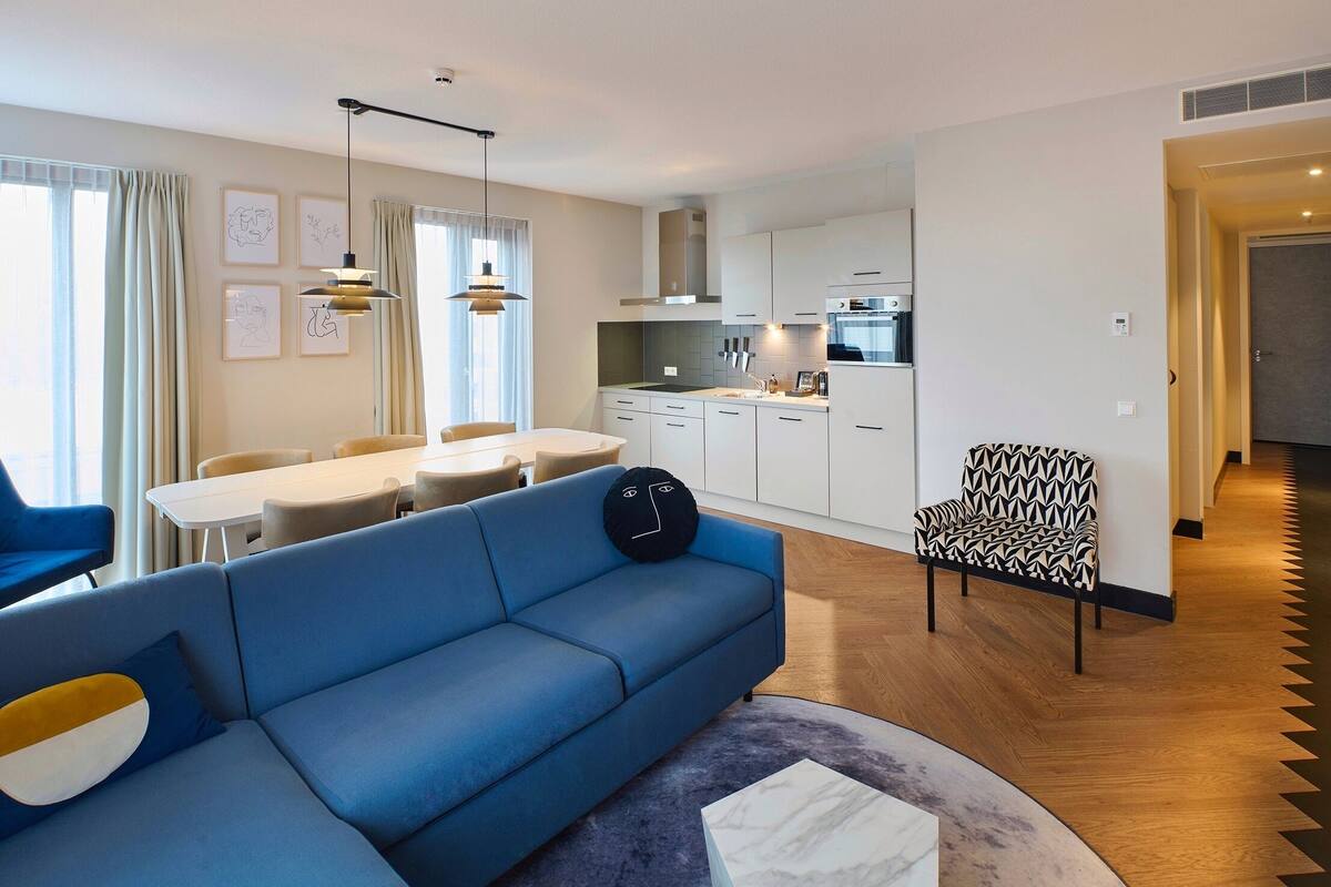 Una sala moderna con un sofá azul, una mesa de comedor y una cocina al fondo.