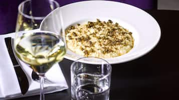 Un plato de comida sobre fondo blanco, acompañado de dos copas de vino blanco y una servilleta.