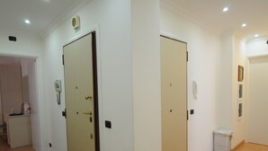 Ein geräumiger Raum mit Holzboden, weißen Wänden und eingelassenen Deckenleuchten. Es gibt zwei Türen, eine mit einem Telefon und die andere mit einem Bilderrahmen.