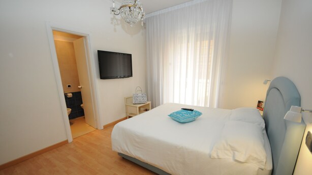 Ein Schlafzimmer mit Bett, einem Wandfernseher, einem Nachttisch und einem Fenster mit Vorhängen.