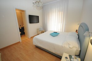 Een slaapkamer met een bed, een aan de muur bevestigde televisie, een nachtkastje en een raam met gordijnen.
