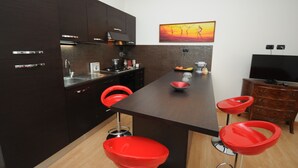 Eine moderne Küche mit dunklen Schränken, einer Holztresle, roten Barhocker und einem Gemälde von Tänzern an der Wand.