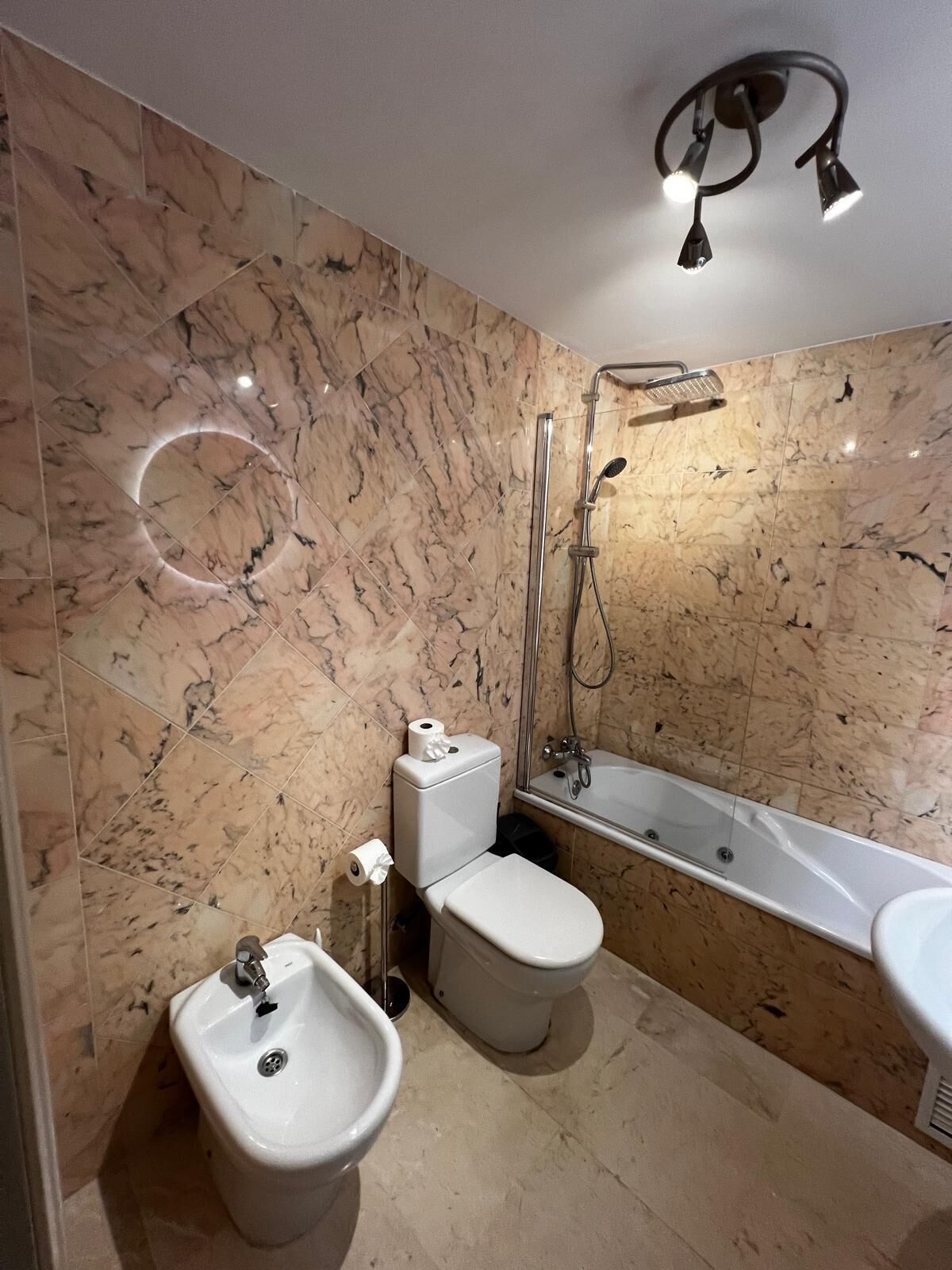 A bathroom with a marble wall, a toilet, a bidet, a sink, and a bathtub.