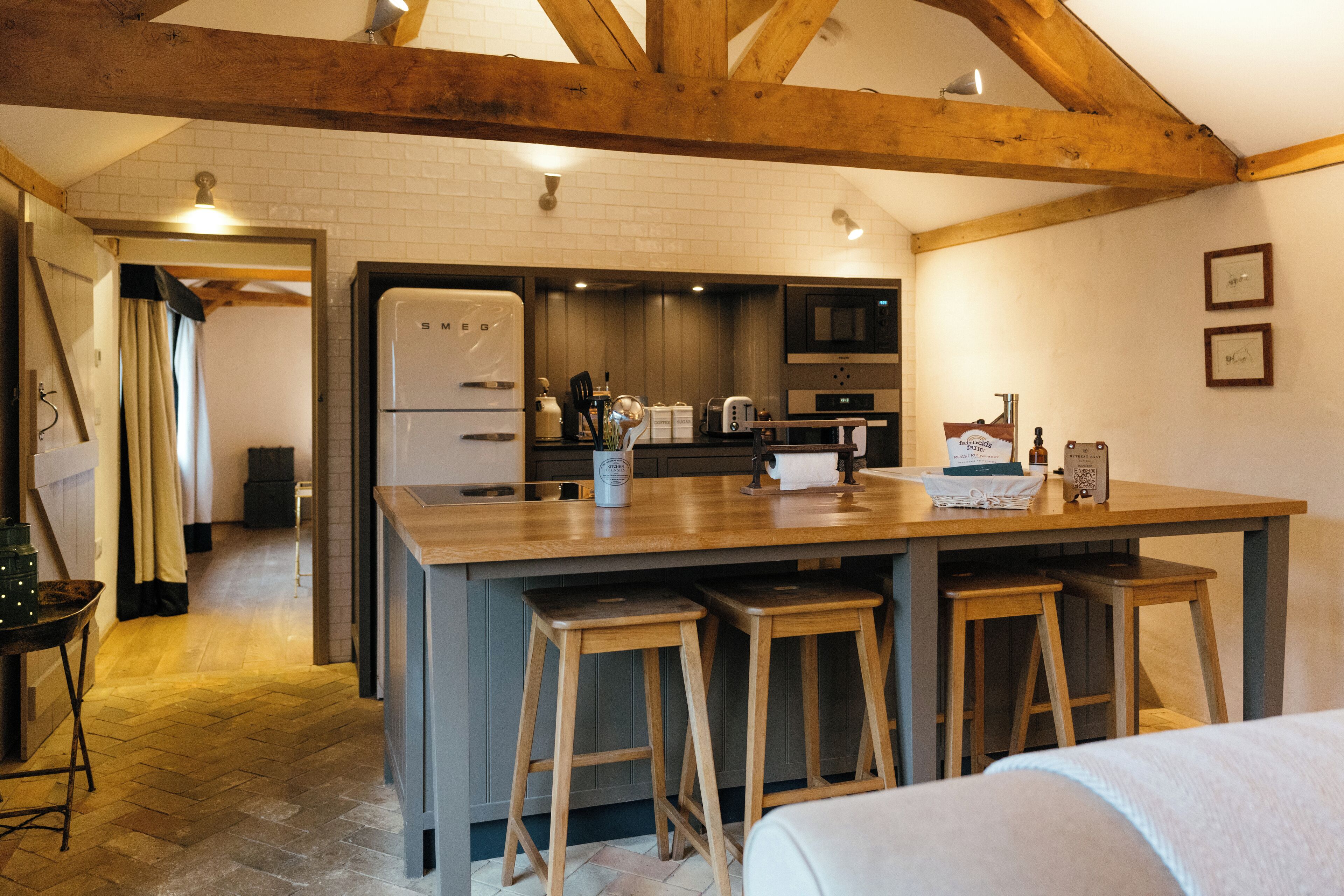 A kitchen with wooden beams, a large island with stools, a refrigerator, and a microwave.