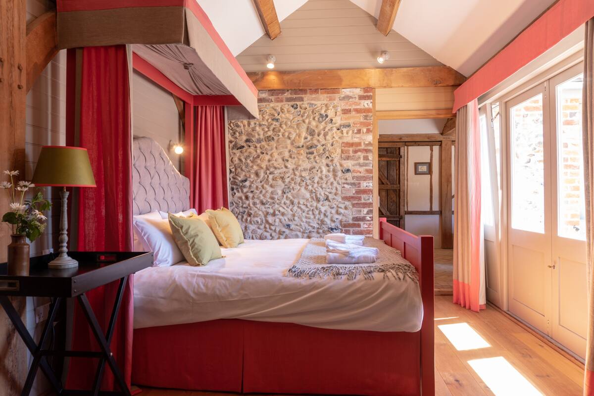A bedroom with a large bed, a nightstand, a lamp, and a stone wall.