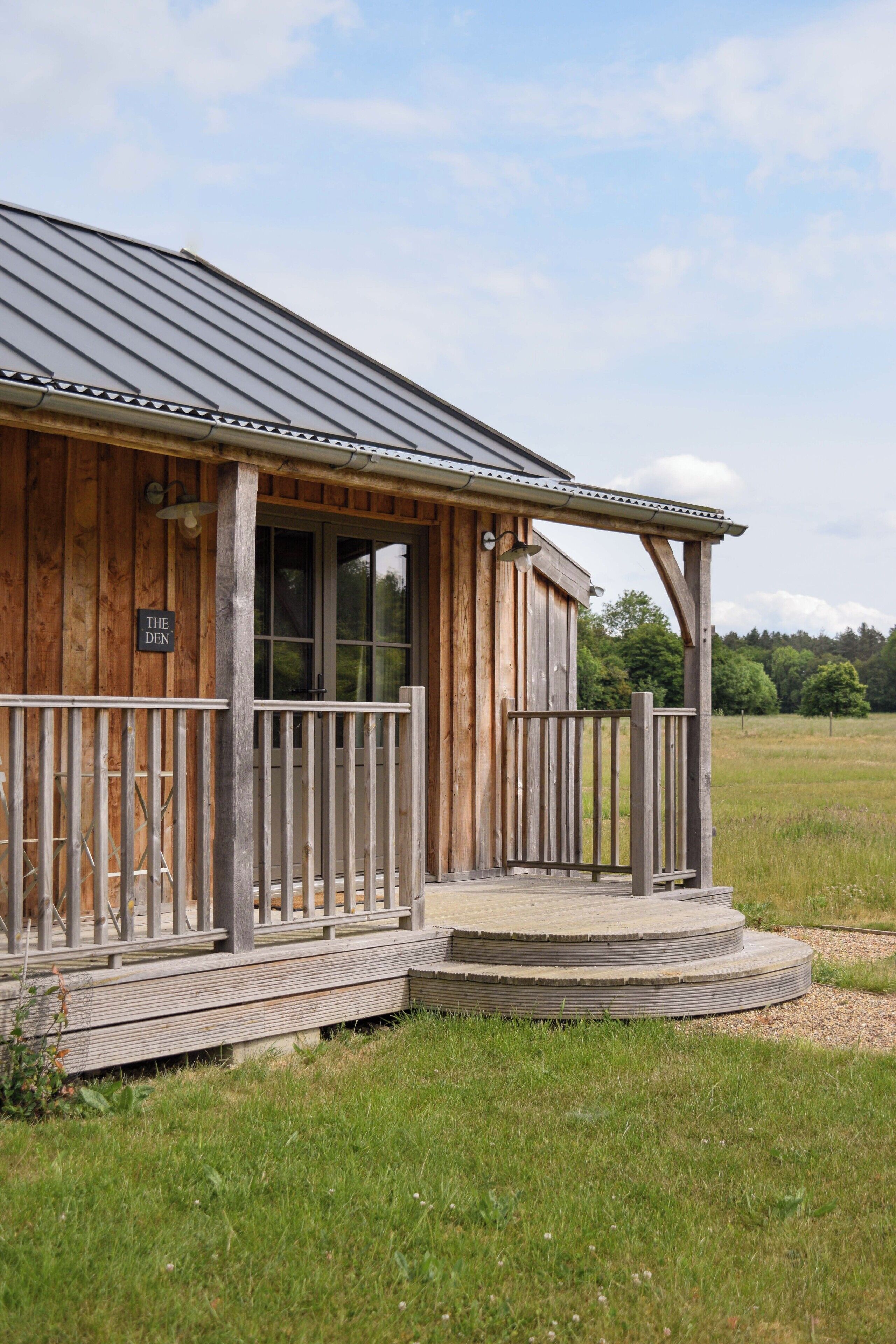 A wooden building with a porch and a sign that reads "THE DEN."