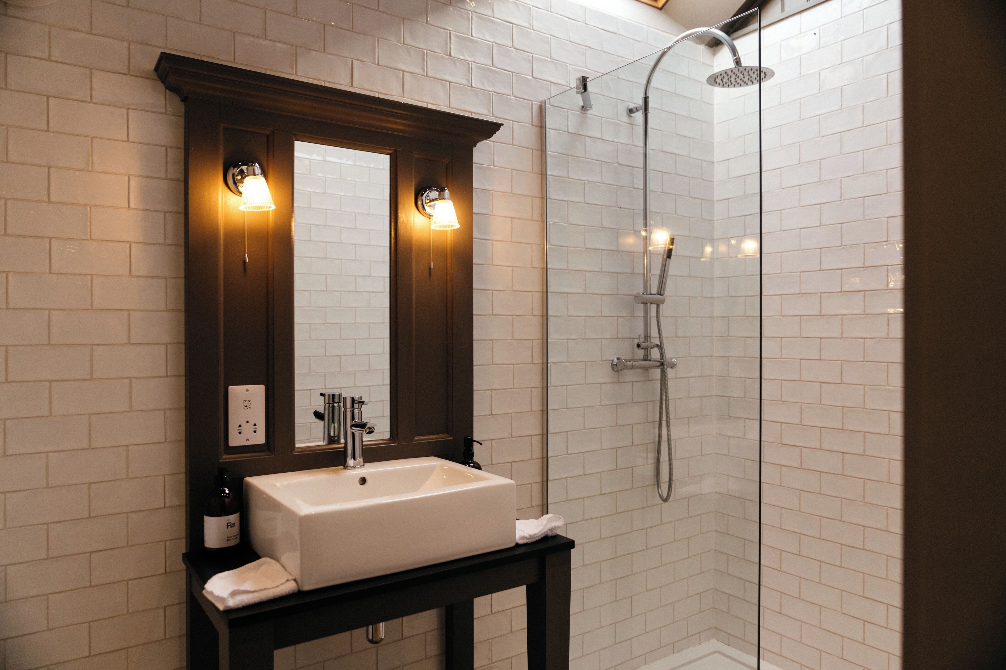 A bathroom with a white sink, dark wooden vanity, and a glass-enclosed shower.