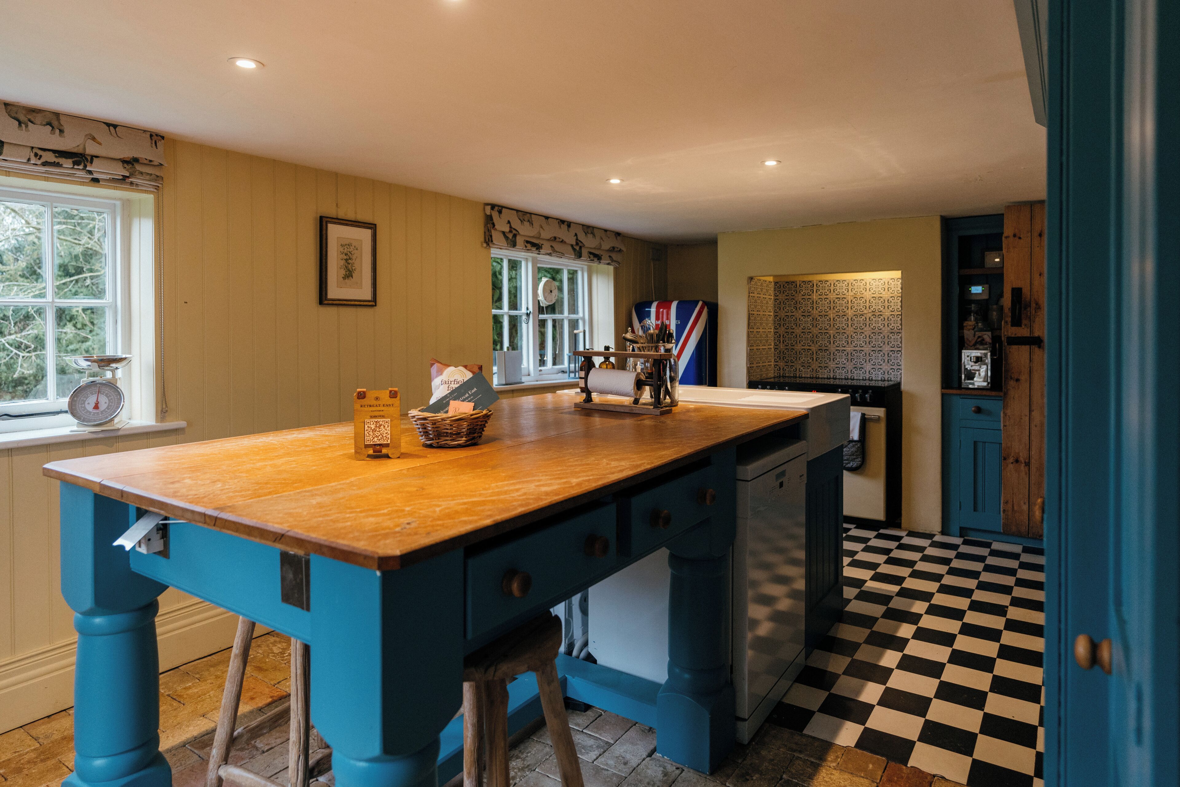 A kitchen with a wooden island, blue cabinetry, a checkered floor, and a window with a view of trees.