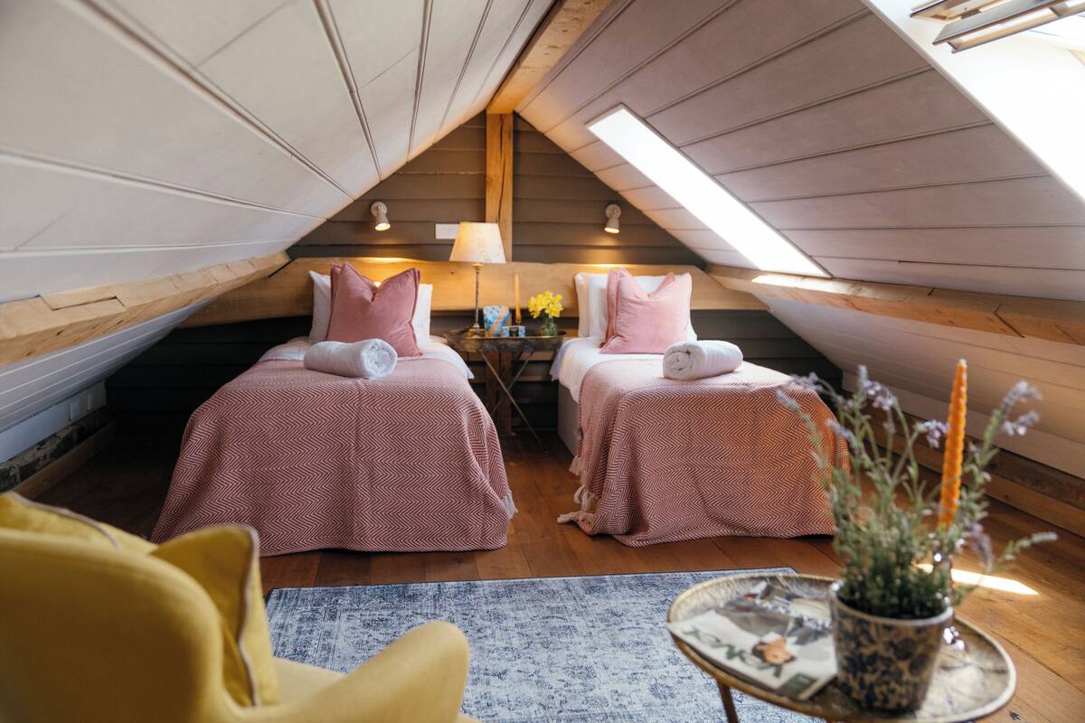 A cozy attic bedroom with two beds, a small table, and a potted plant.