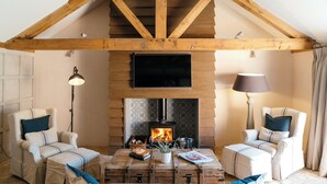 A cozy living room with a fireplace, two armchairs, a wooden coffee table, and a television above the fireplace. - Retreat East (Ipswich)