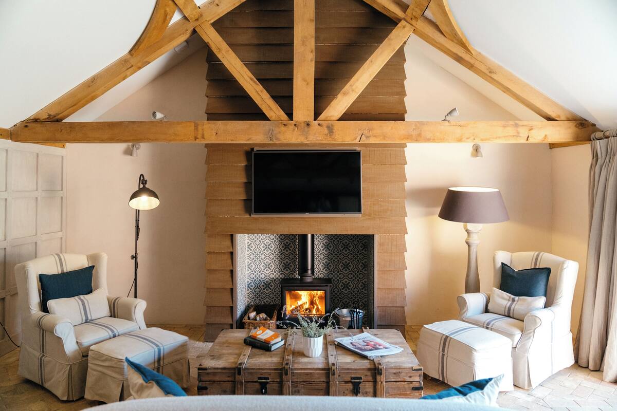 A cozy living room with a fireplace, two armchairs, a wooden coffee table, and a television above the fireplace.