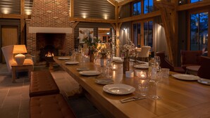A long dining table set for a meal with a fireplace, wooden beams, and large windows. - Retreat East (Ipswich)