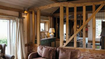 A rustic interior with exposed wooden beams, a leather sofa, a vintage trunk as a coffee table, and a chandelier.