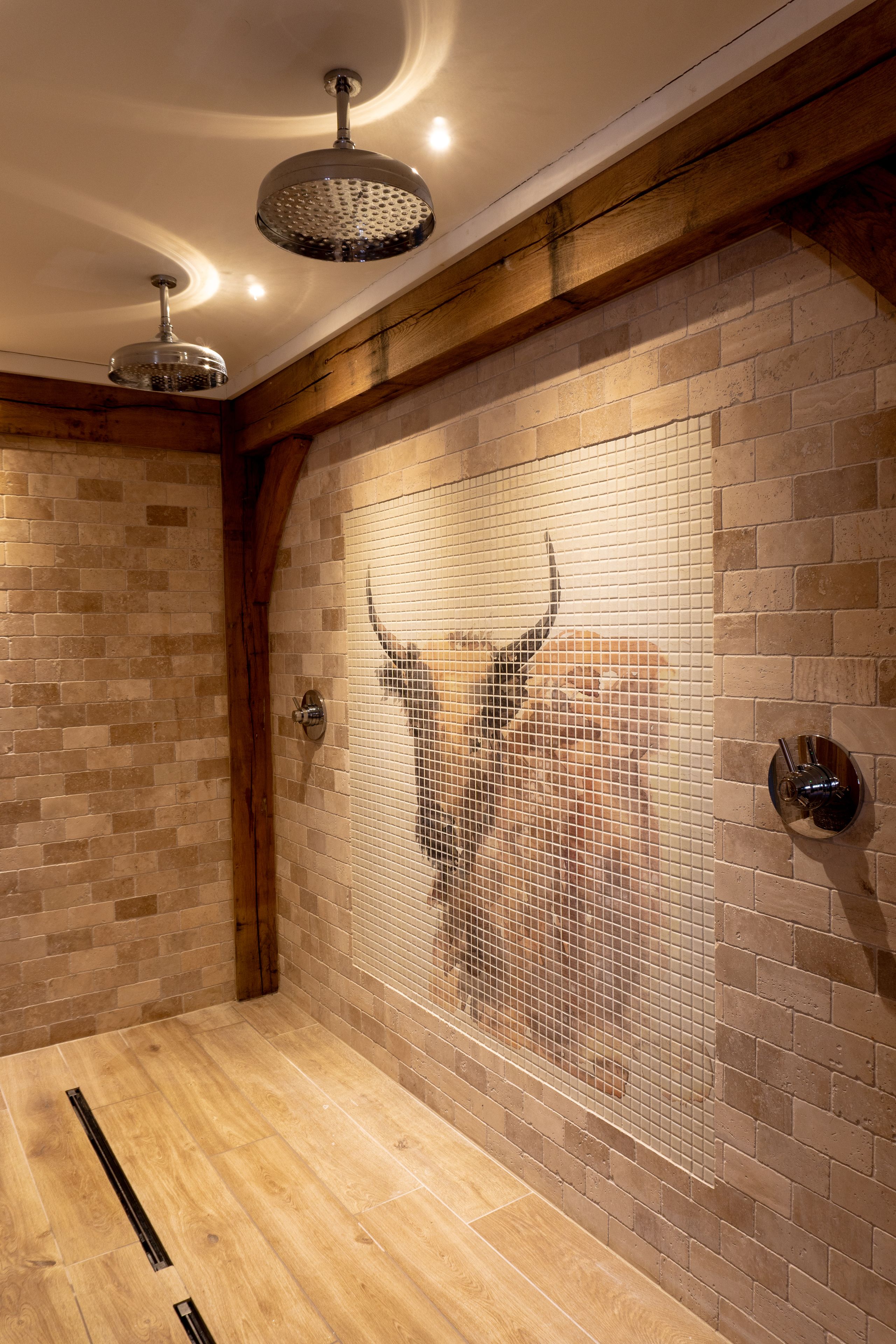 A bathroom with a wooden floor, a tiled wall with a bull's head design, and two ceiling-mounted showerheads.