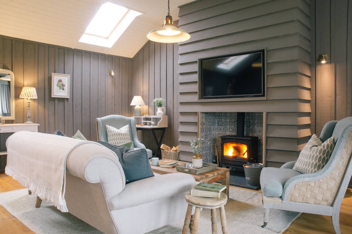 A cozy living room with a fireplace, comfortable seating, and a television mounted on the wall.