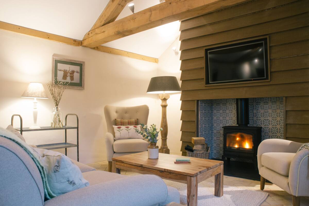 A cozy living room with a fireplace, a sofa, a coffee table, and a TV mounted on the wall.