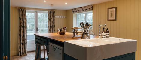 A kitchen with a large island, wooden stools, a sink, and a window with curtains.
