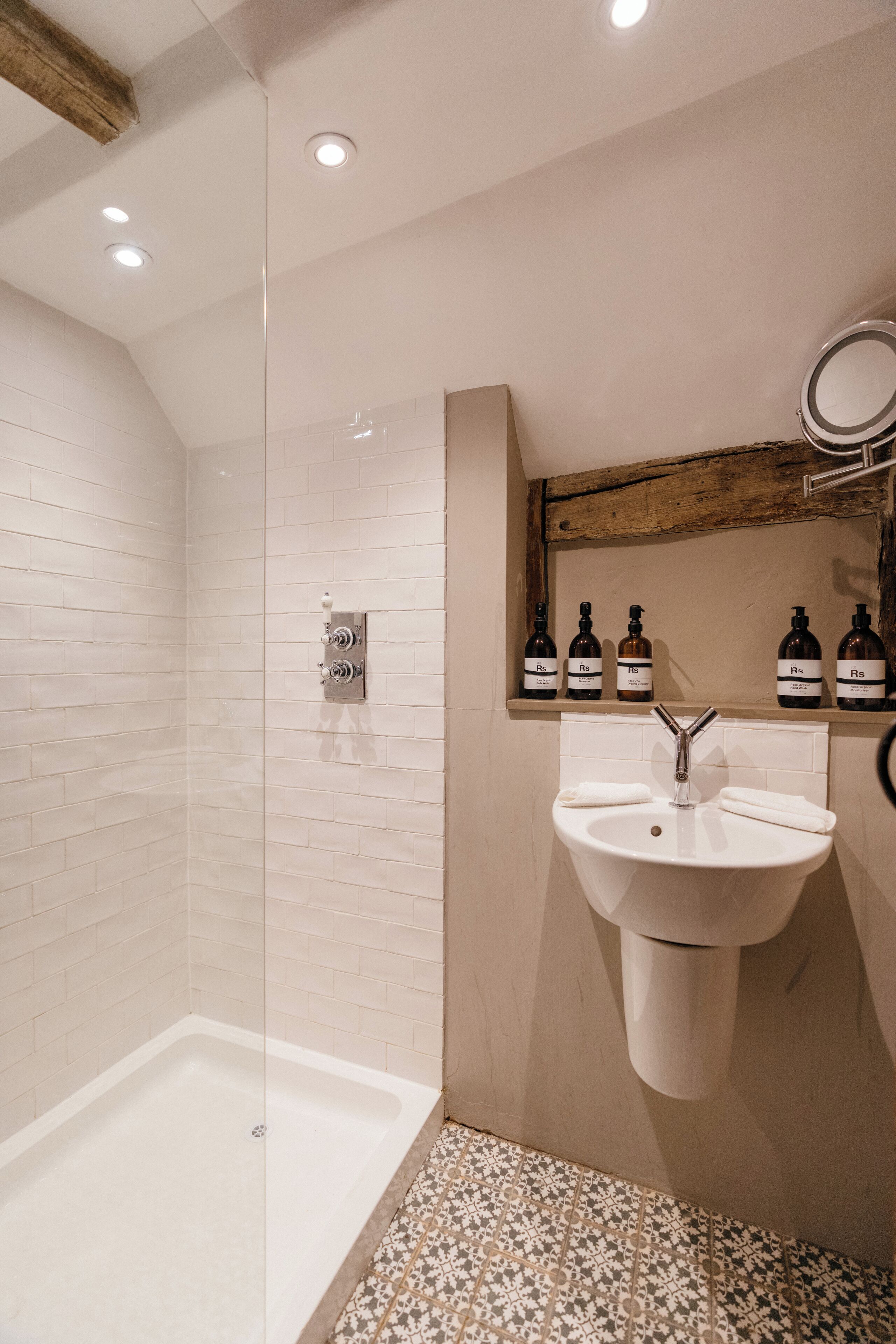 Een moderne badkamer met een douchecabine van glas, een witte wastafel met spiegel erboven en een plank met toiletartikelen.