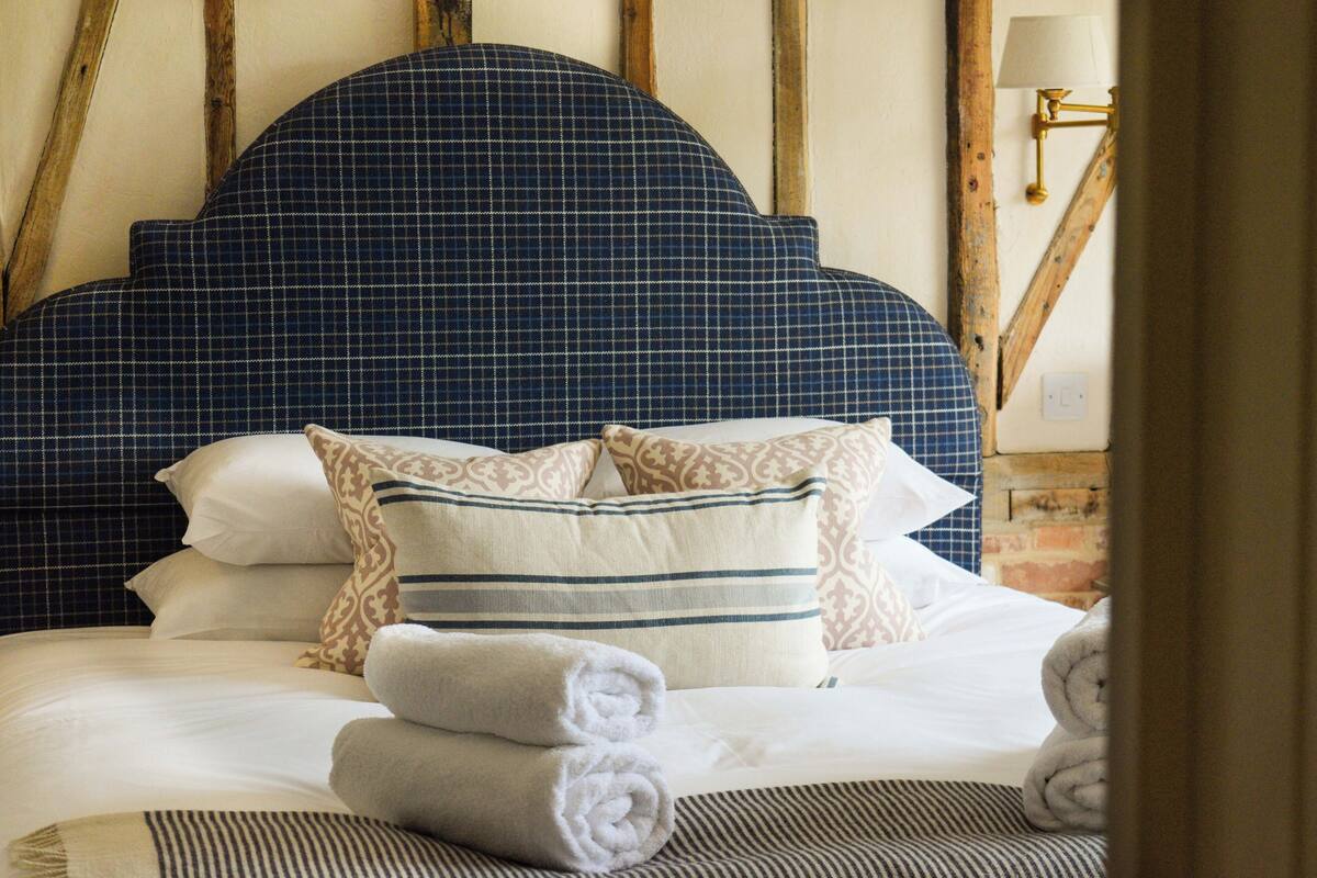 A neatly made bed with a checkered headboard, patterned pillows, and rolled towels.