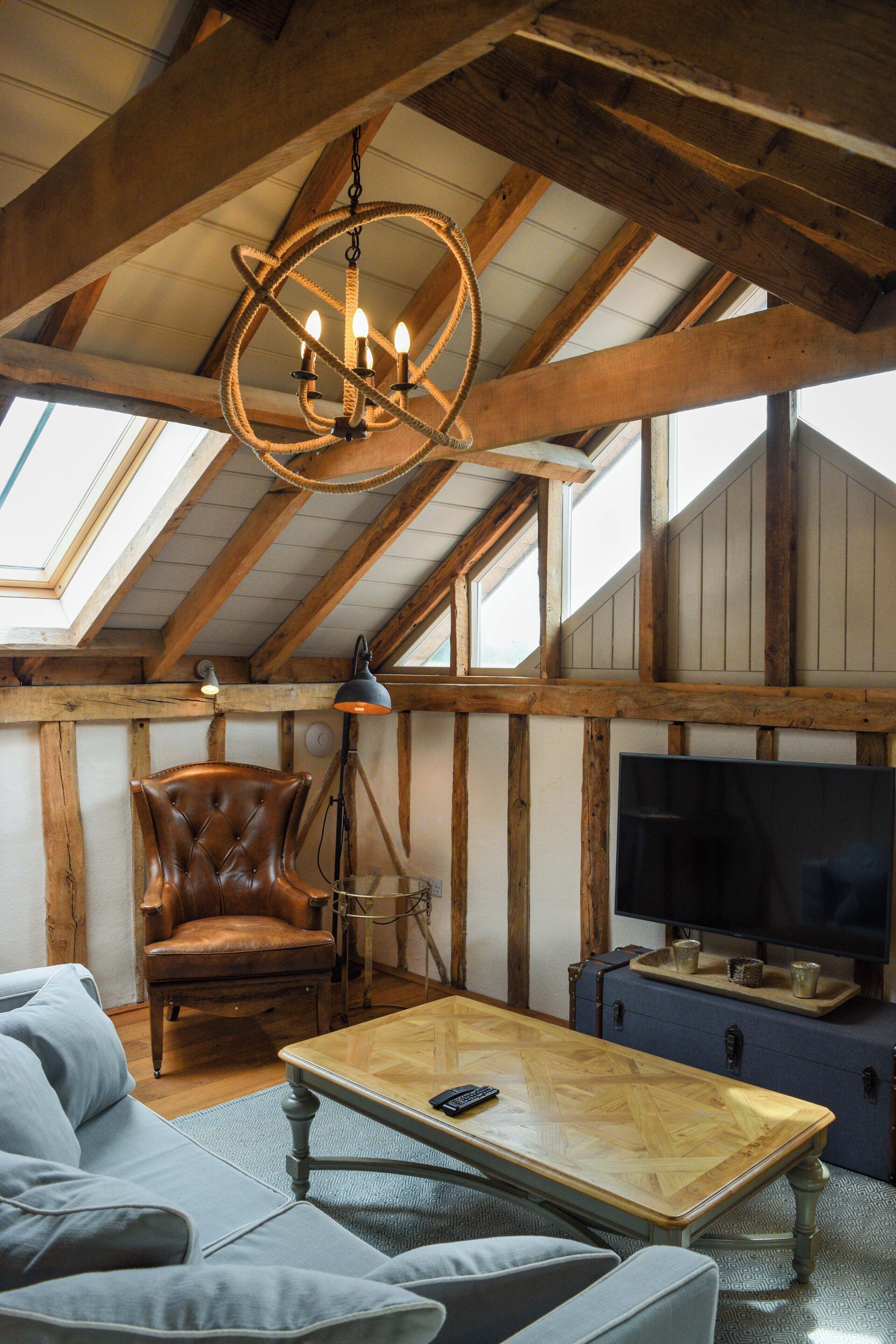 Un acogedor espacio tipo loft con techo de madera, un sillón de cuero, un televisor y un ventanal grande.