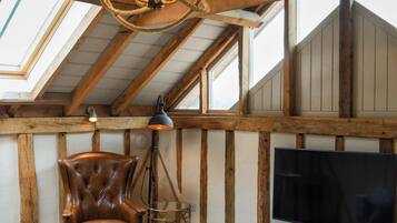 Un acogedor espacio tipo loft con techo de madera, un sillón de cuero, un televisor y un ventanal grande.