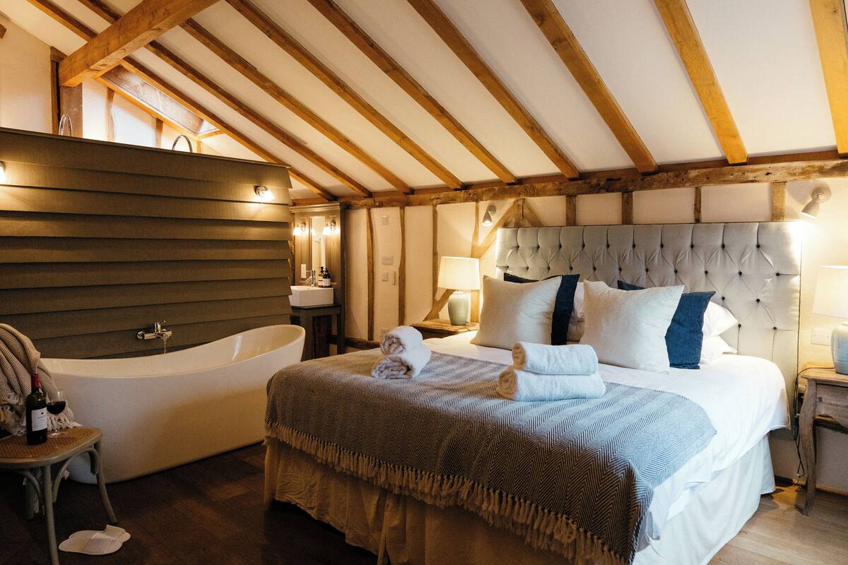 A bedroom with a large bed, a bathtub, wooden beams, and a wooden floor.