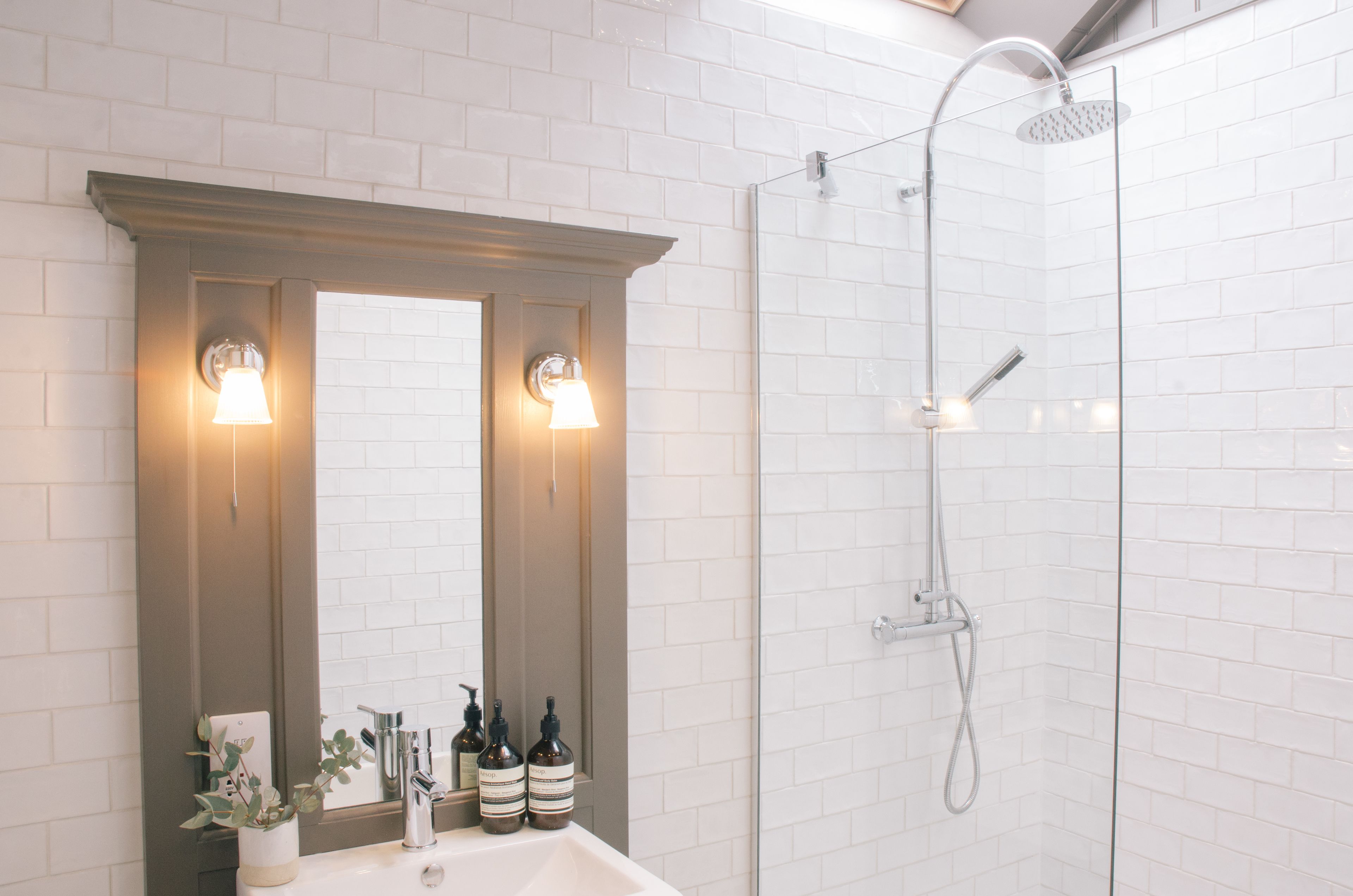 Un bagno con doccia rivestita di piastrelle bianche, un lavabo con specchio e due luci a parete.