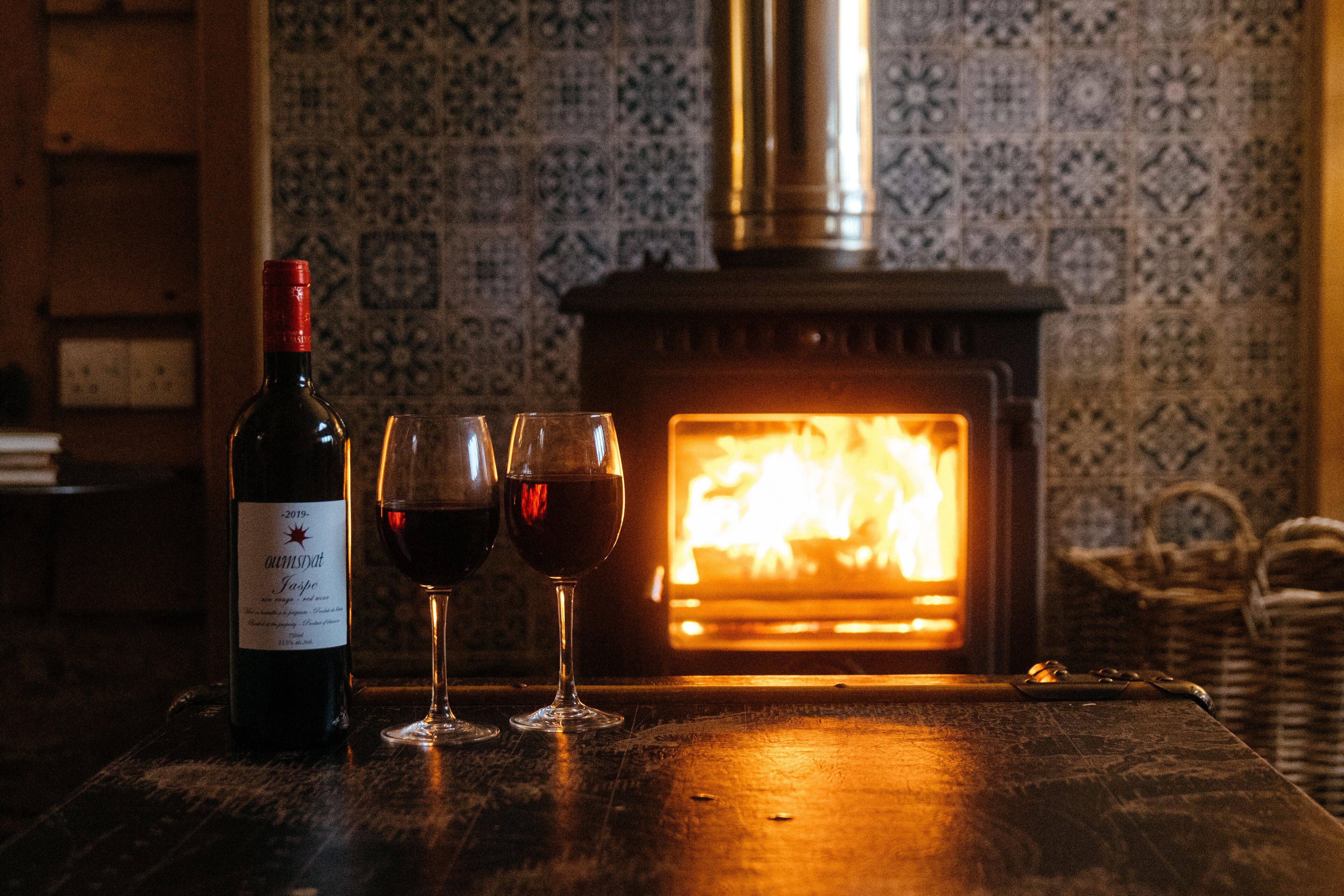 Una botella de vino y dos copas sobre una mesa de madera frente a una chimenea.