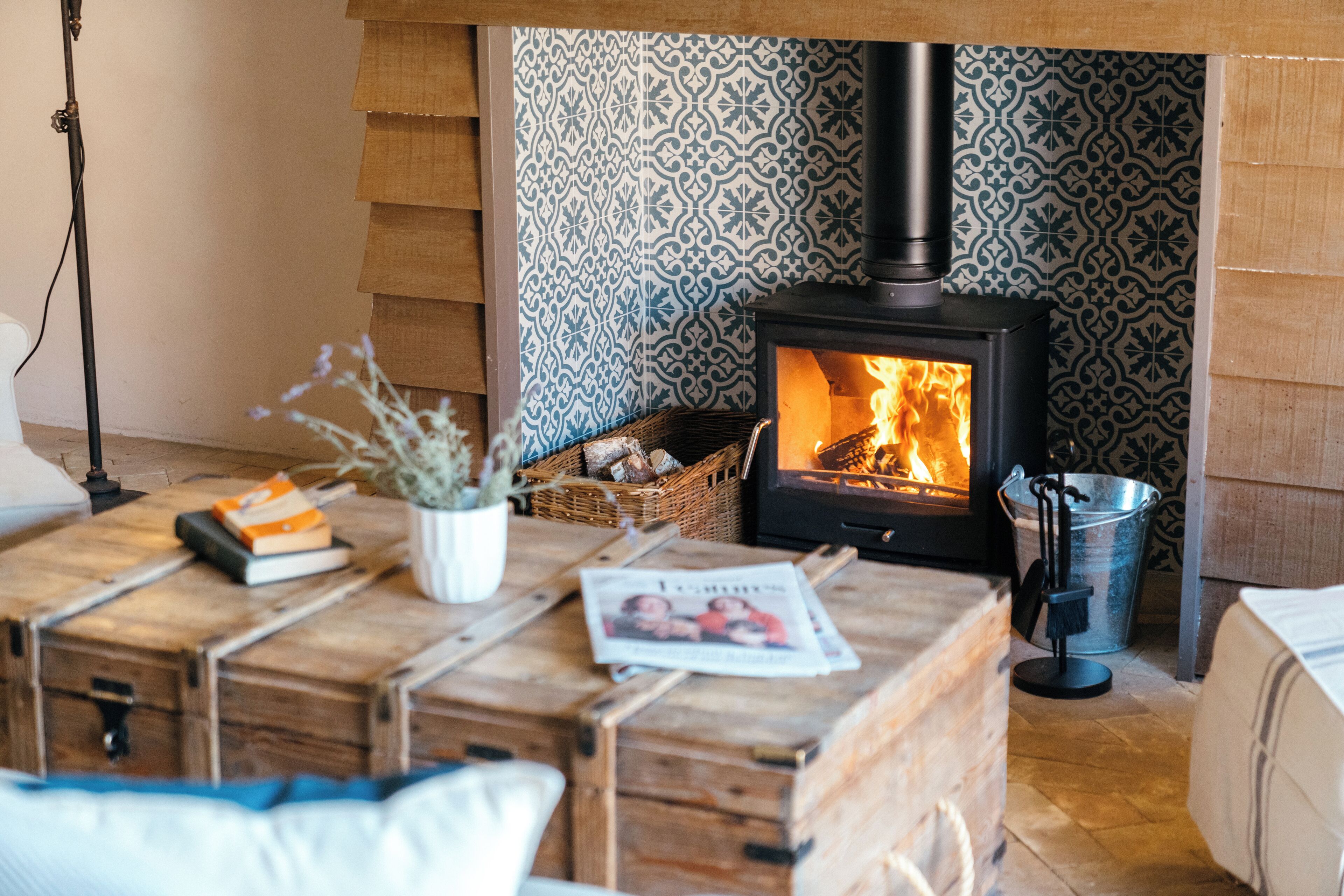 Une pièce chaleureuse avec un poêle à bois, une malle en bois, un panier de bois de chauffage et un seau en métal.