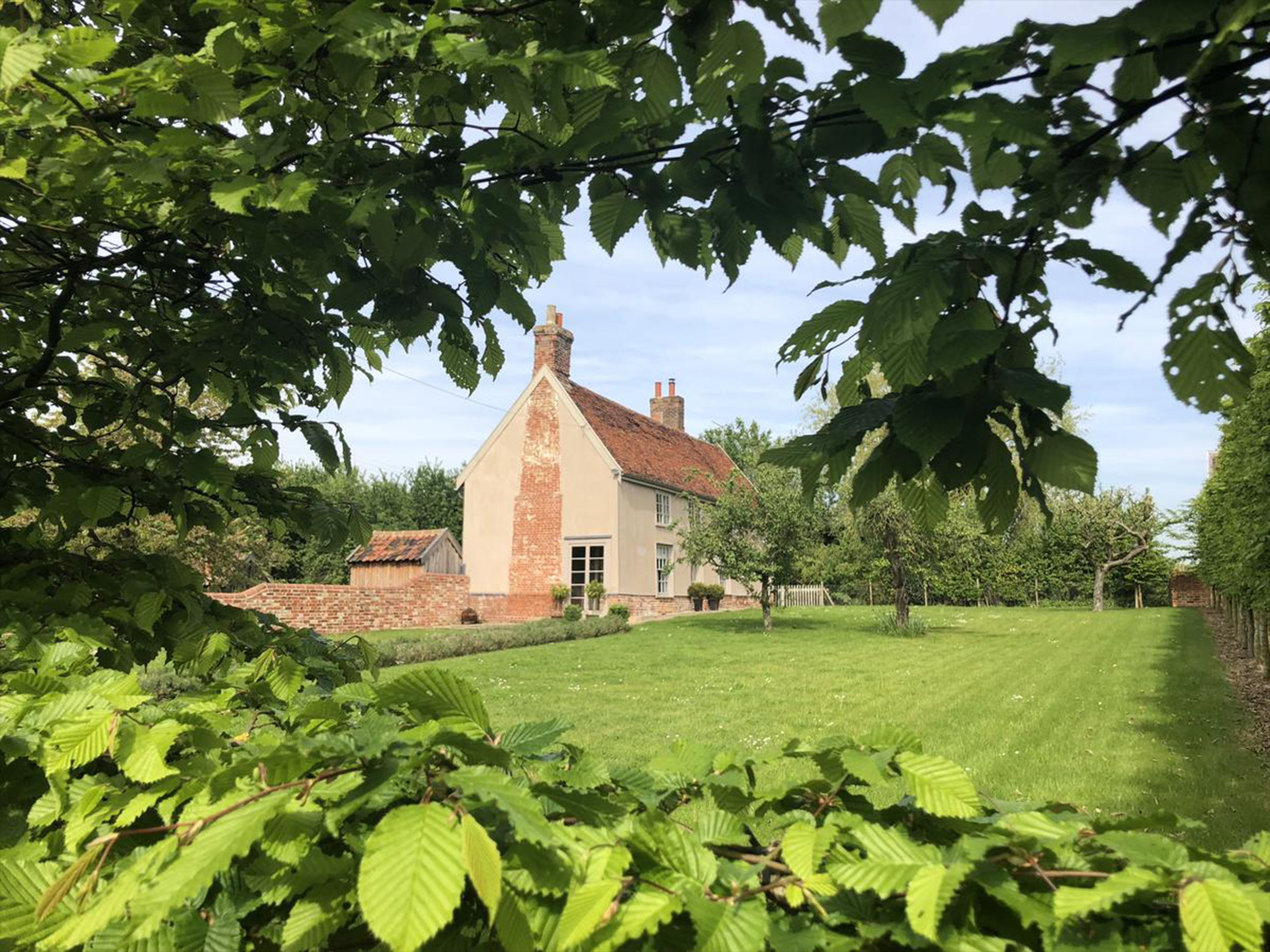 A traditional house with a brick chimney, surrounded by a well-maintained lawn and dense foliage.