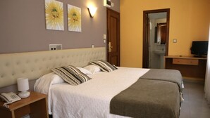 Habitación de hotel con una cama grande, una mesita de noche con un teléfono, una lámpara y un televisor sobre un soporte de madera.