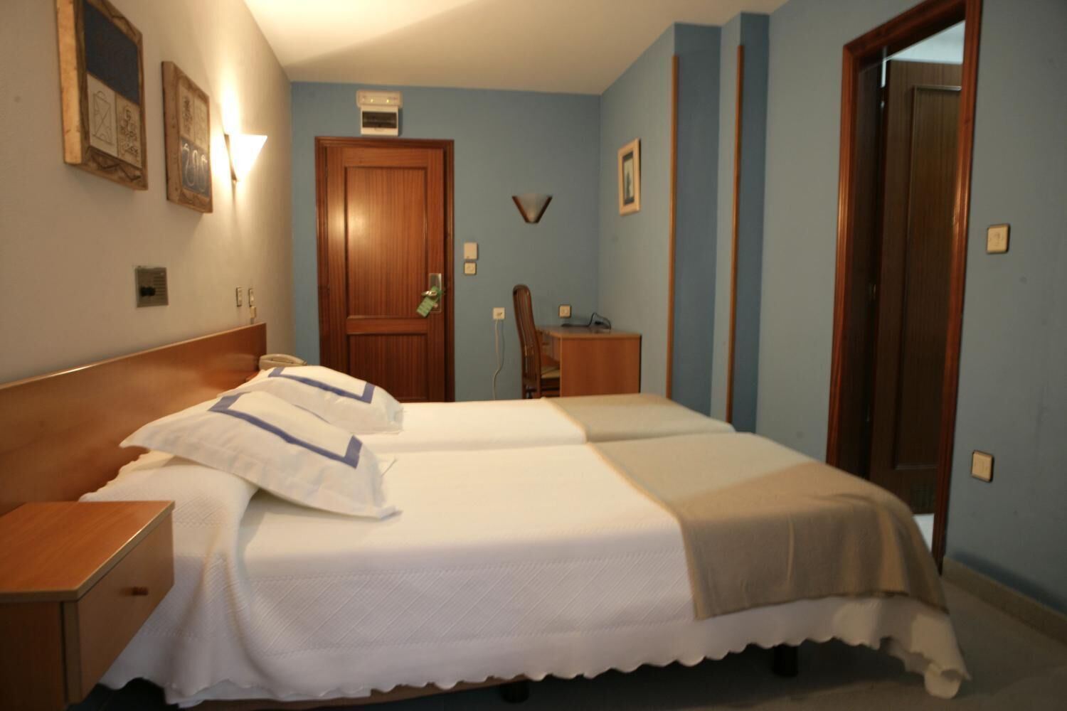 A hotel room with two beds, a wooden headboard, a desk, and a chair.