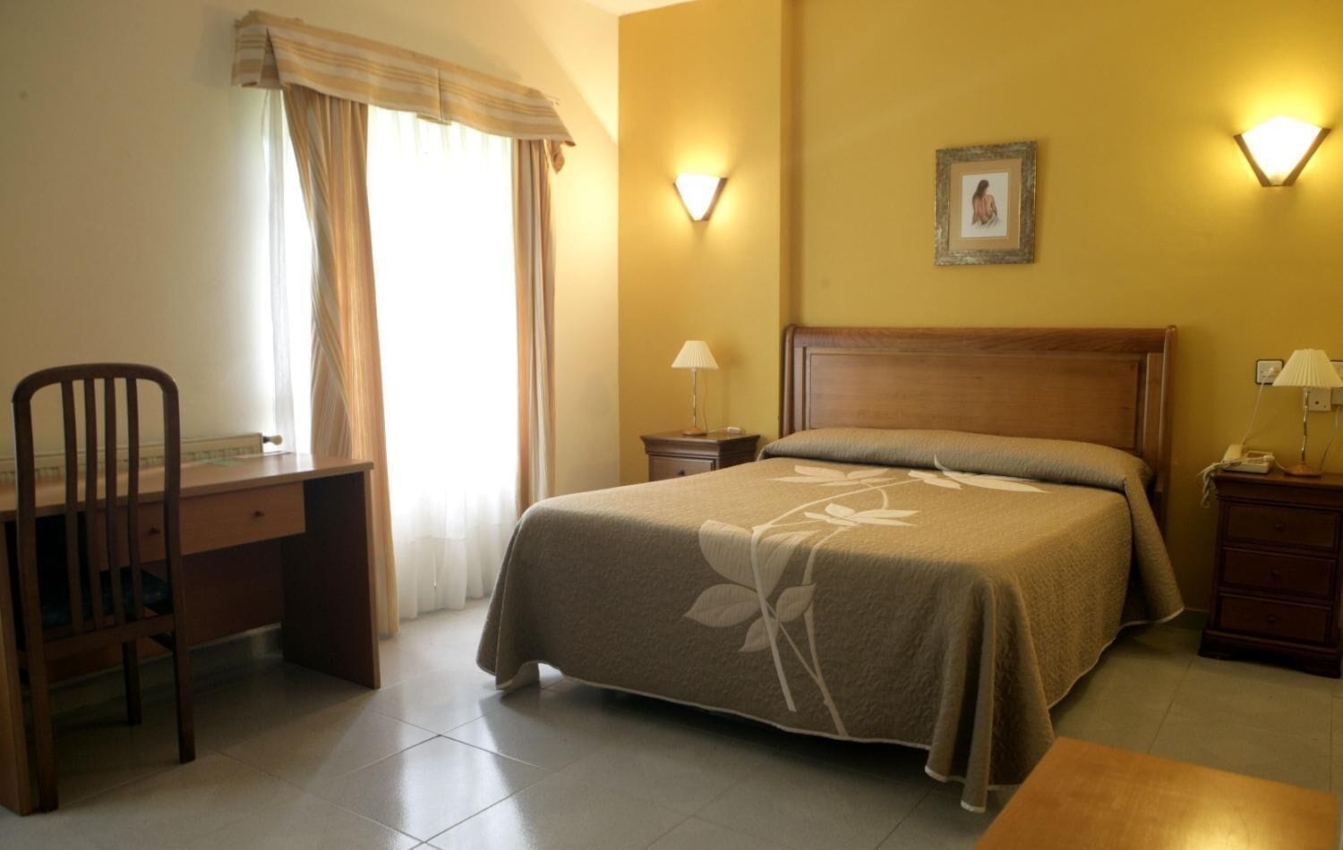 Una habitación de hotel con cama, escritorio, silla, mesita de noche y lámpara.