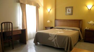 Una habitación de hotel con cama, escritorio, silla, mesita de noche y lámpara.