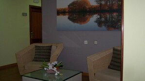 Una habitación con dos sillones de mimbre, una mesita de centro de vidrio y un arreglo floral, además de un cuadro grande que representa un lago.