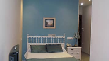Un dormitorio con cama, mesita de noche con lámpara, teléfono y televisor.