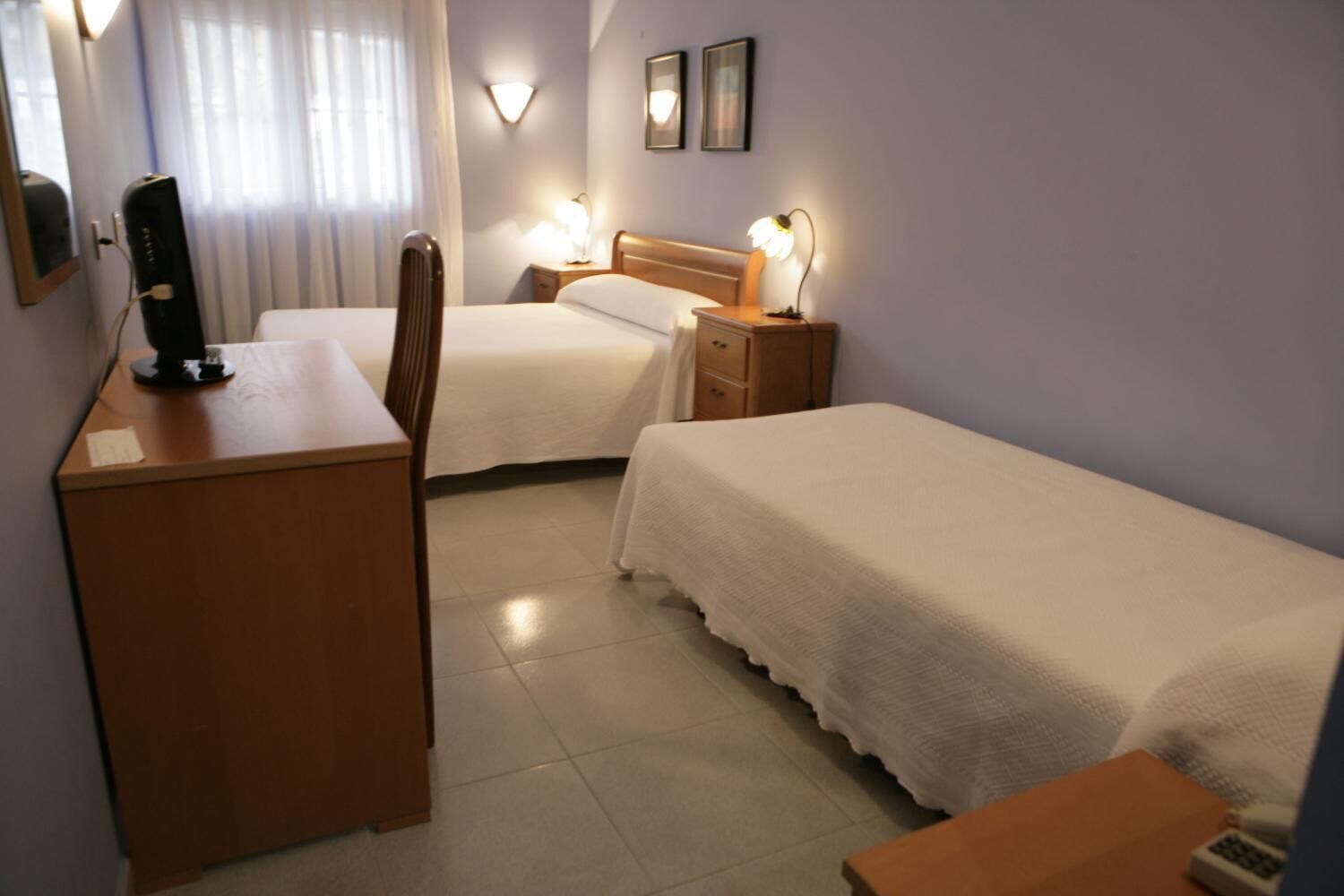 Ein Hotelzimmer mit Schreibtisch, zwei Betten, einem Sessel, einem Nachttisch mit Lampen und einem Spiegel.