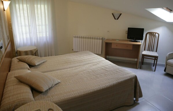 Un dormitorio con una cama grande, un escritorio, una silla, un radiador y un televisor.