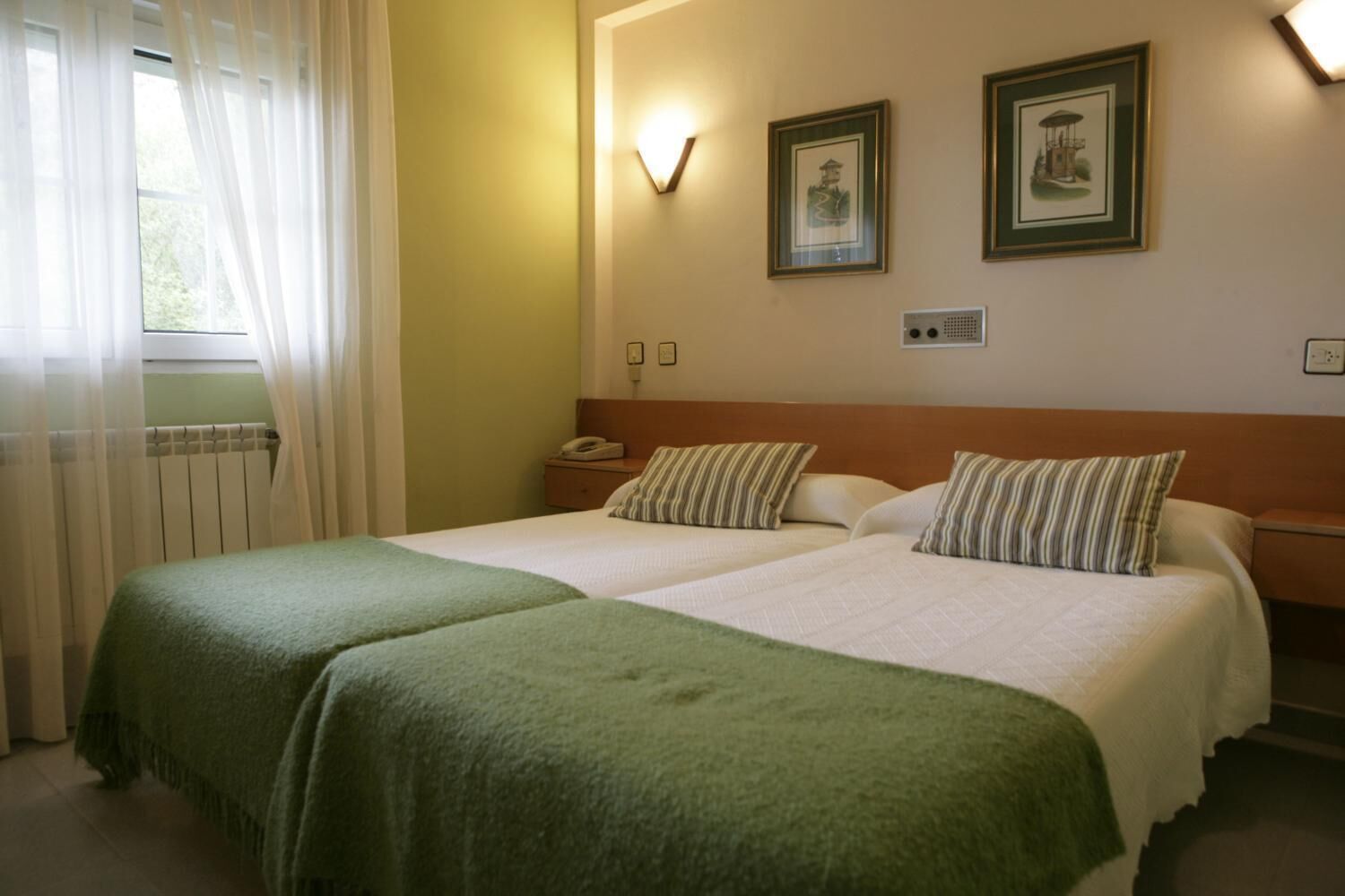 Habitació d'hotel amb dos llits, una tauleta de nit, un telèfon i dues imatges emmarcades a la paret.