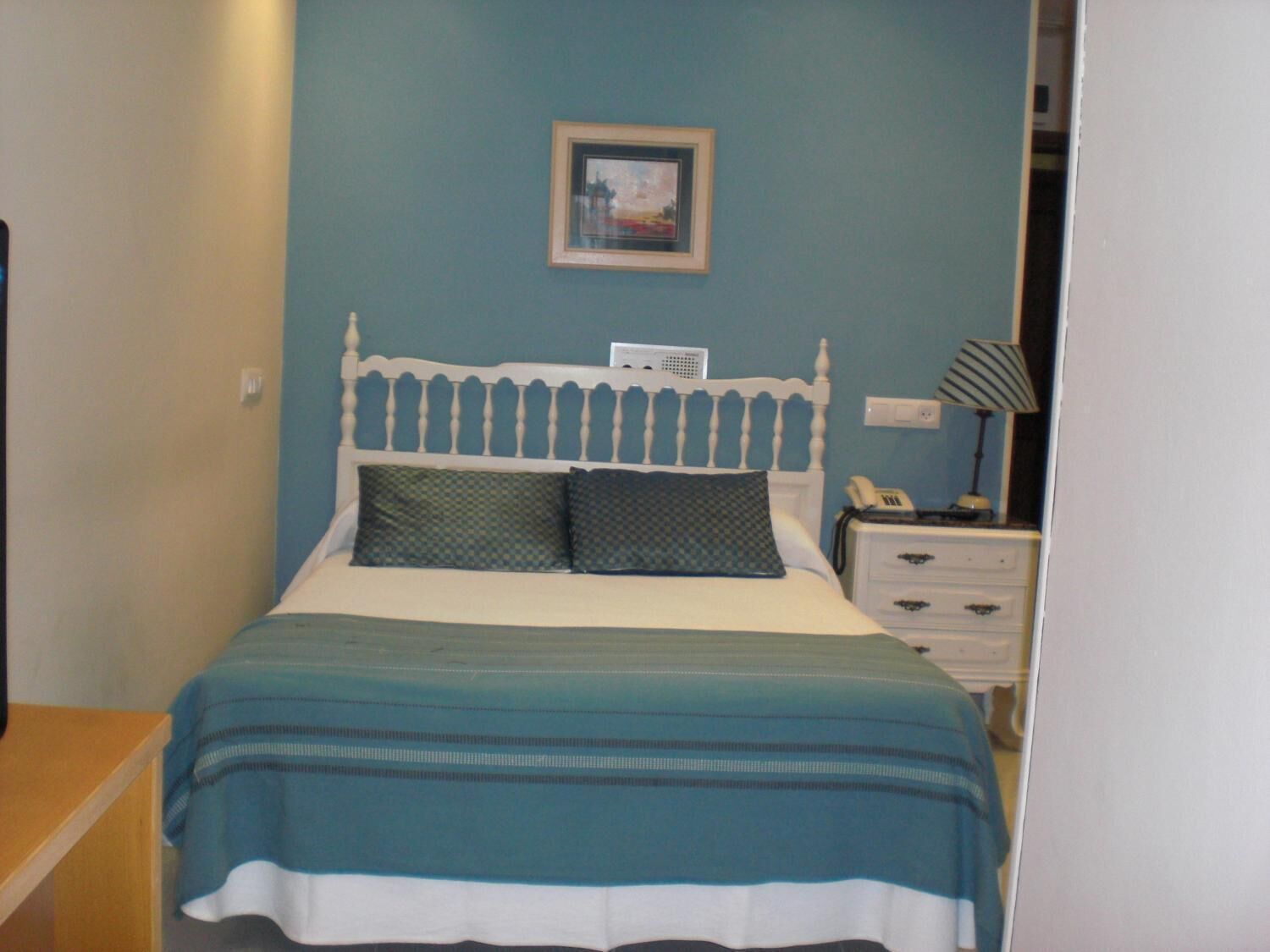 Une chambre à coucher avec un lit, une table de chevet, une lampe et un tableau encadré au mur.