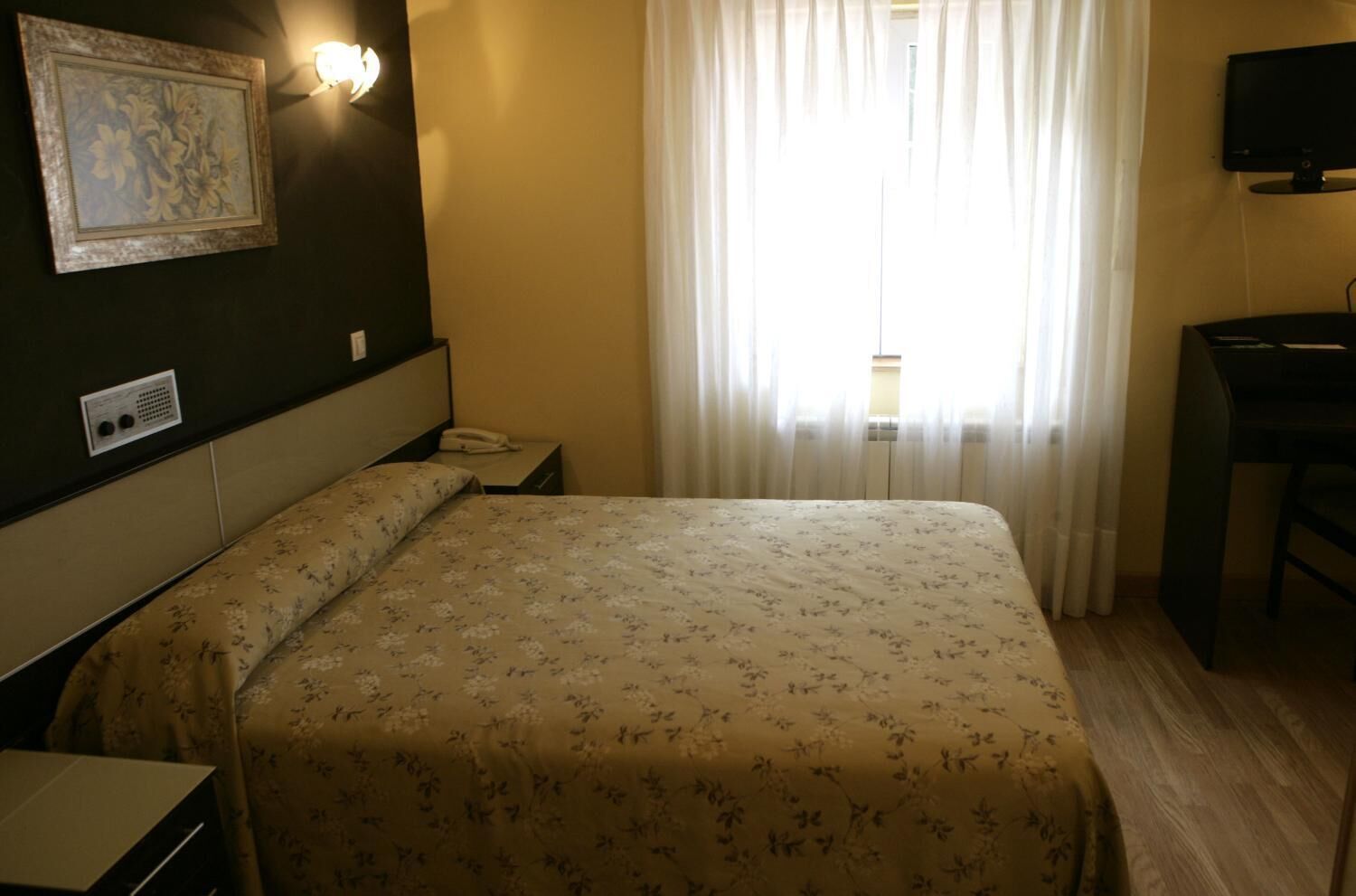 Habitación de hotel con cama, escritorio, silla, teléfono y televisión montada en la pared.