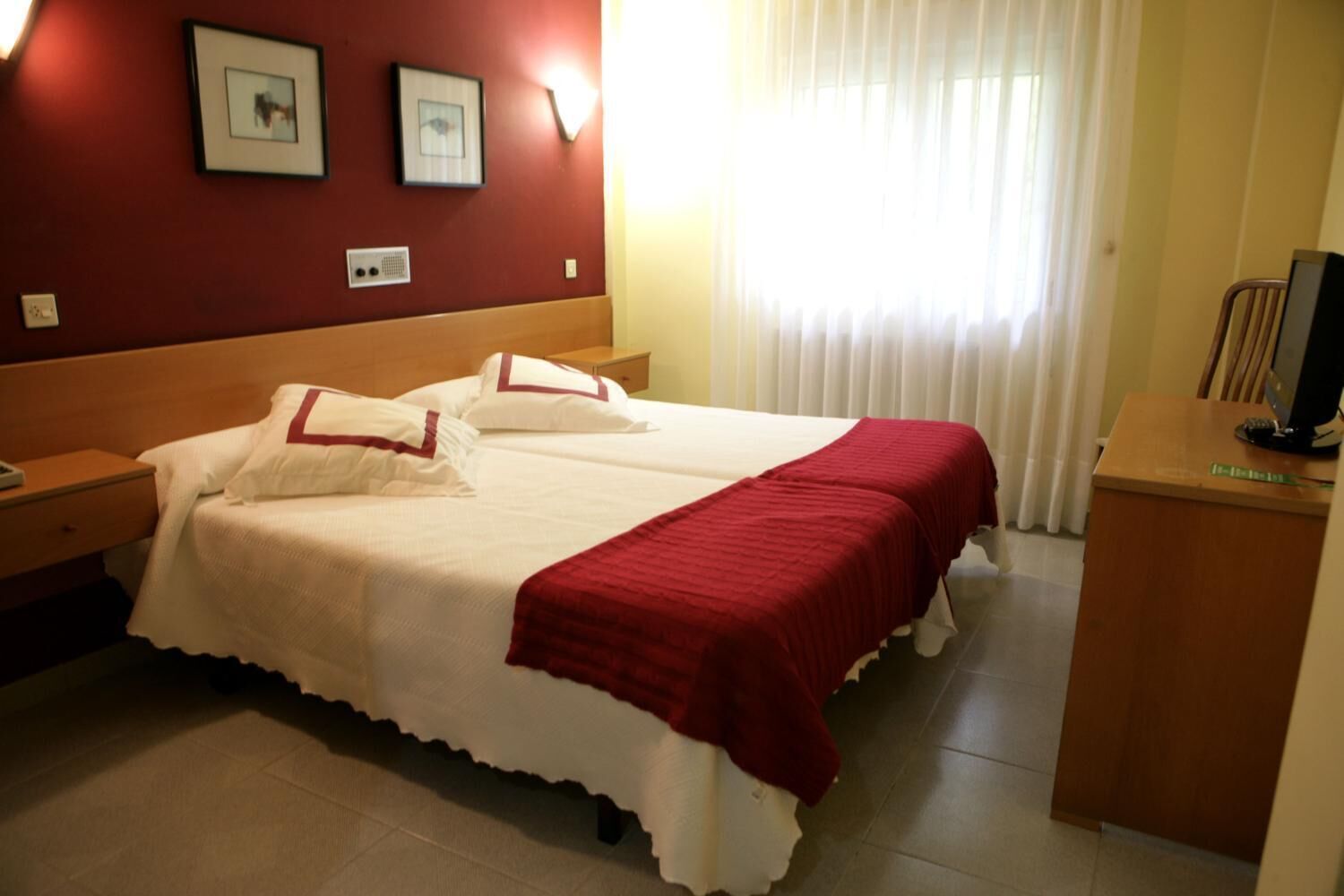 Habitación de hotel con una cama grande, dos mesitas de noche, un escritorio con una computadora y una ventana con cortinas.