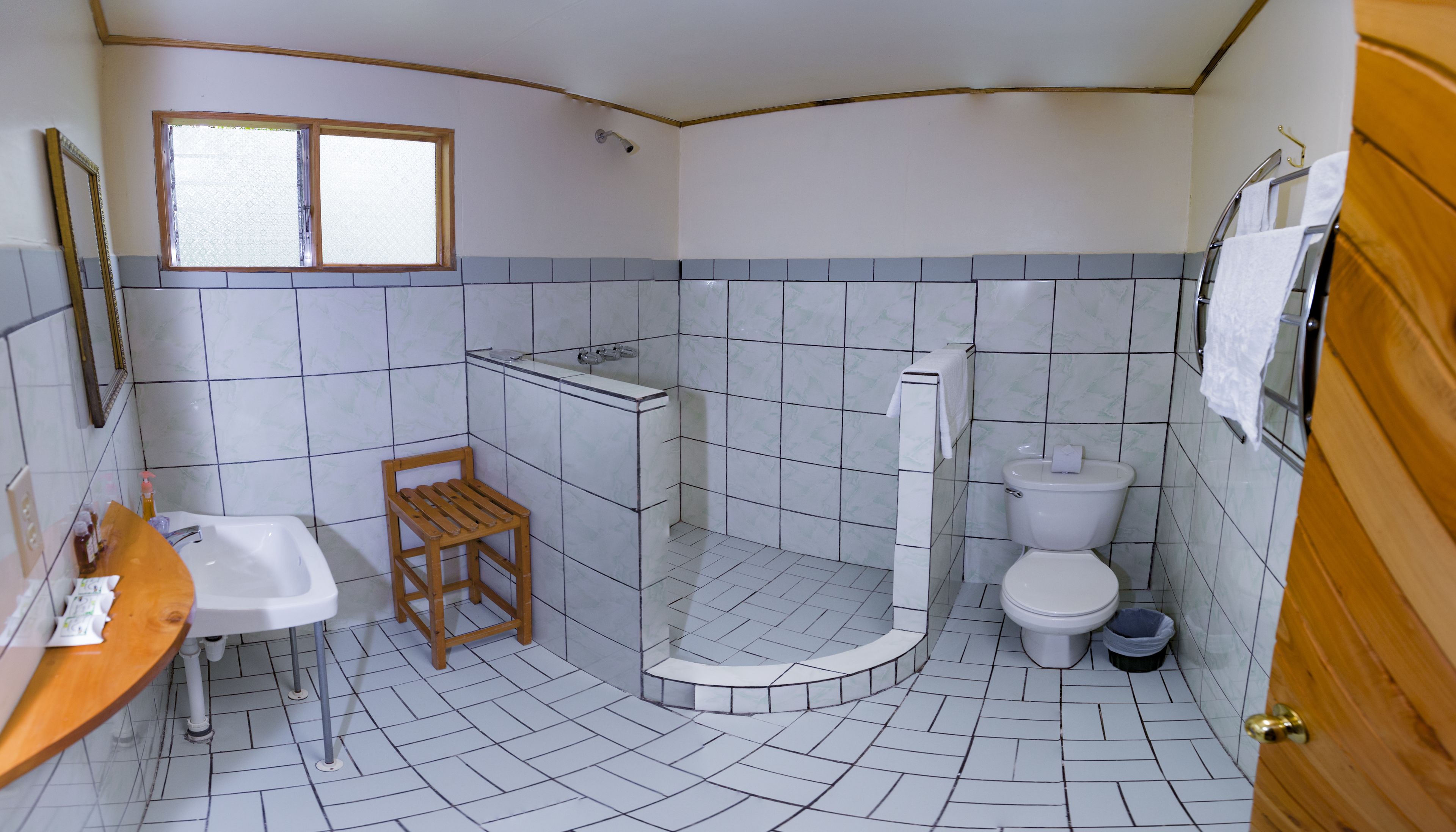 Un baño con ducha, inodoro, lavabo y un taburete pequeño de madera.