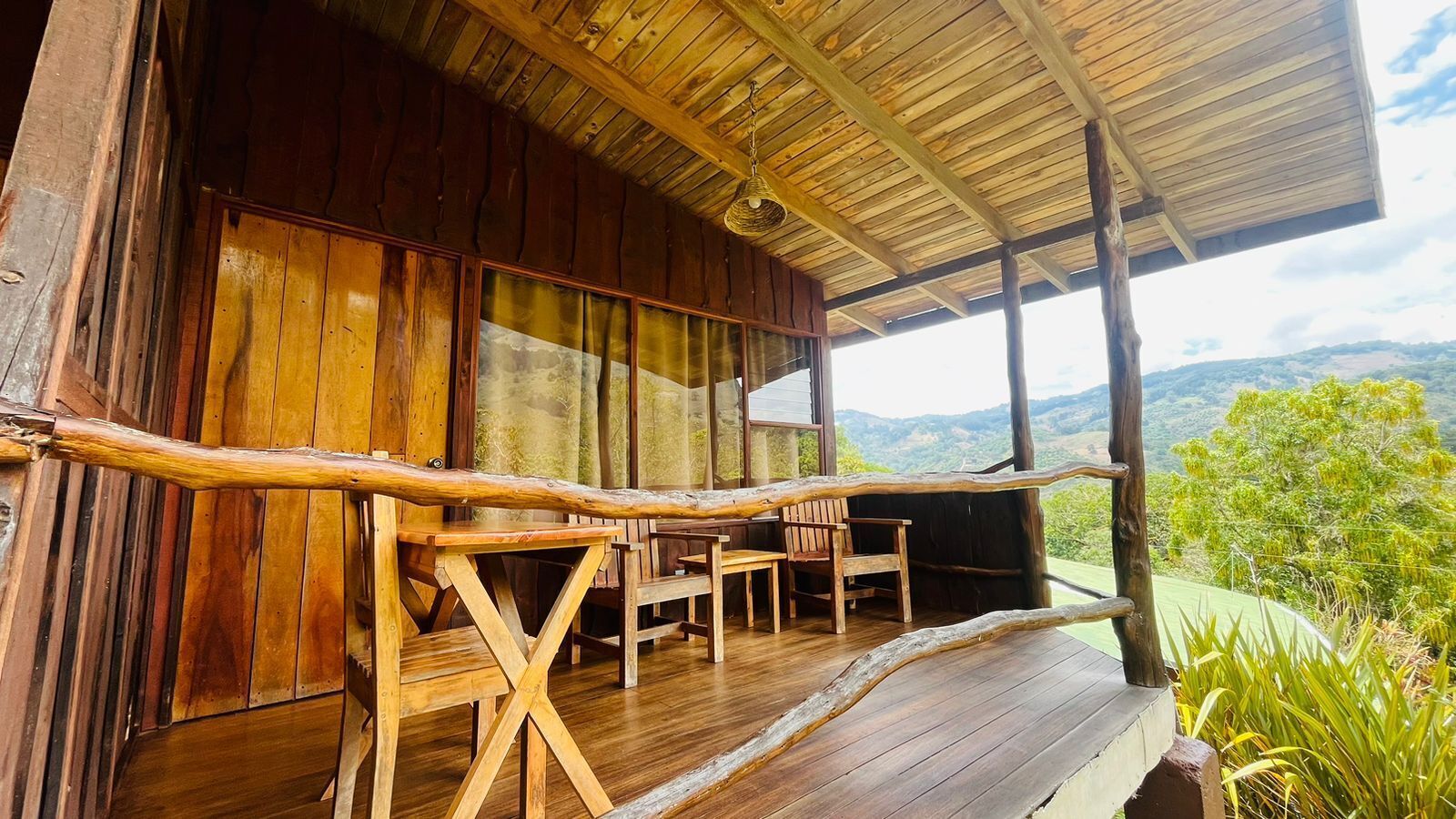 Una terraza de madera con un diseño rústico, que incluye una mesa y sillas de madera, y vistas del paisaje circundante.
