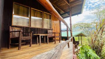 A wooden cabin with a porch, large windows, and a view of the mountains.