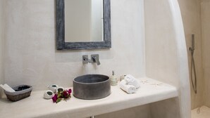 Une salle de bain avec un grand miroir, un lavabo rond, une douche et une petite étagère contenant des articles de toilette.