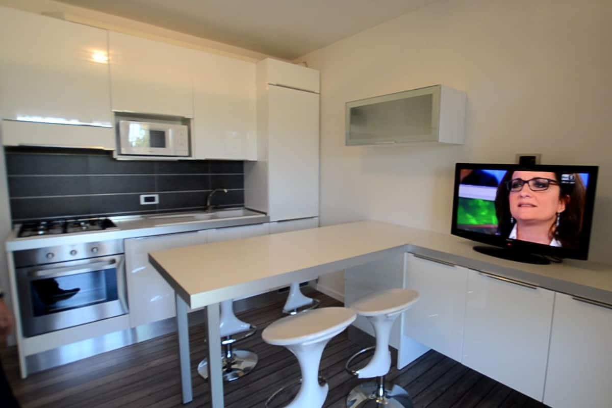 A modern kitchen with white cabinets, a microwave, a stove, and a TV mounted on the wall.