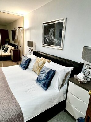 Une chambre d’hôtel avec un lit, une table de chevet, une lampe, un tableau encadré au mur et un miroir.