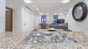 A modern kitchen with a granite countertop, stainless steel stove, and a dining area with a gray sofa and a TV. - Mayfair Piccadilly Apartment (London)