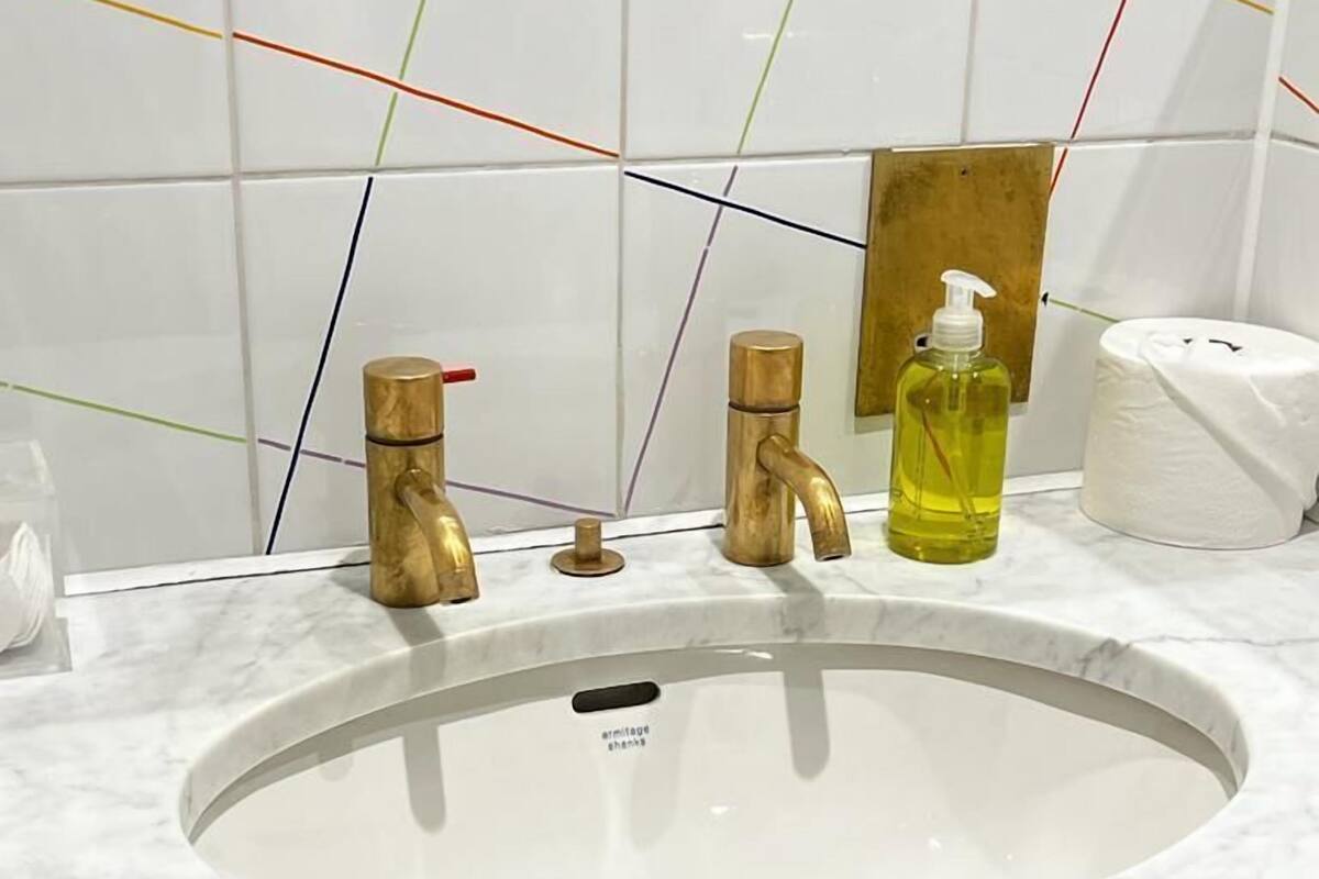 Et badeværelse med en hvid vask, to guldfarvede vandhaner, en sæbedispenser og toiletpapir.